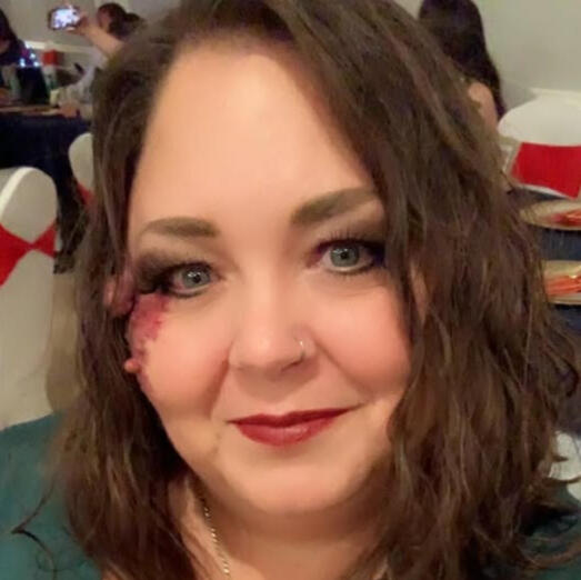 Headshot of Heidi Joyce, a woman of white skin with shoulder-length brown hair. wearing makeup and red lipstick.